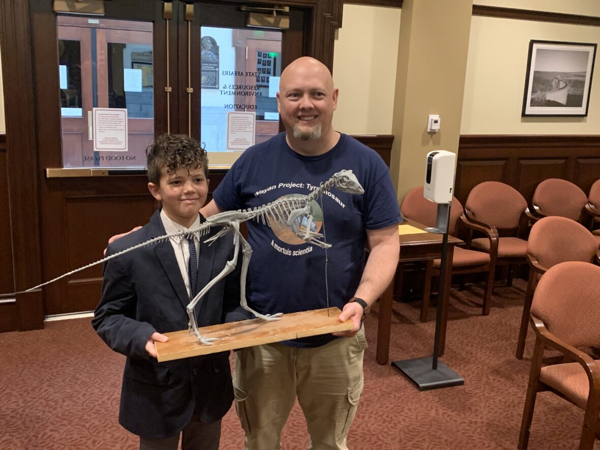 Idaho Falls fourth-grader Levi Herway and professor L.J. Krumenacker stand with a model of the oryctodromeus after Friday morning’s Senate State Affairs Committee hearing.